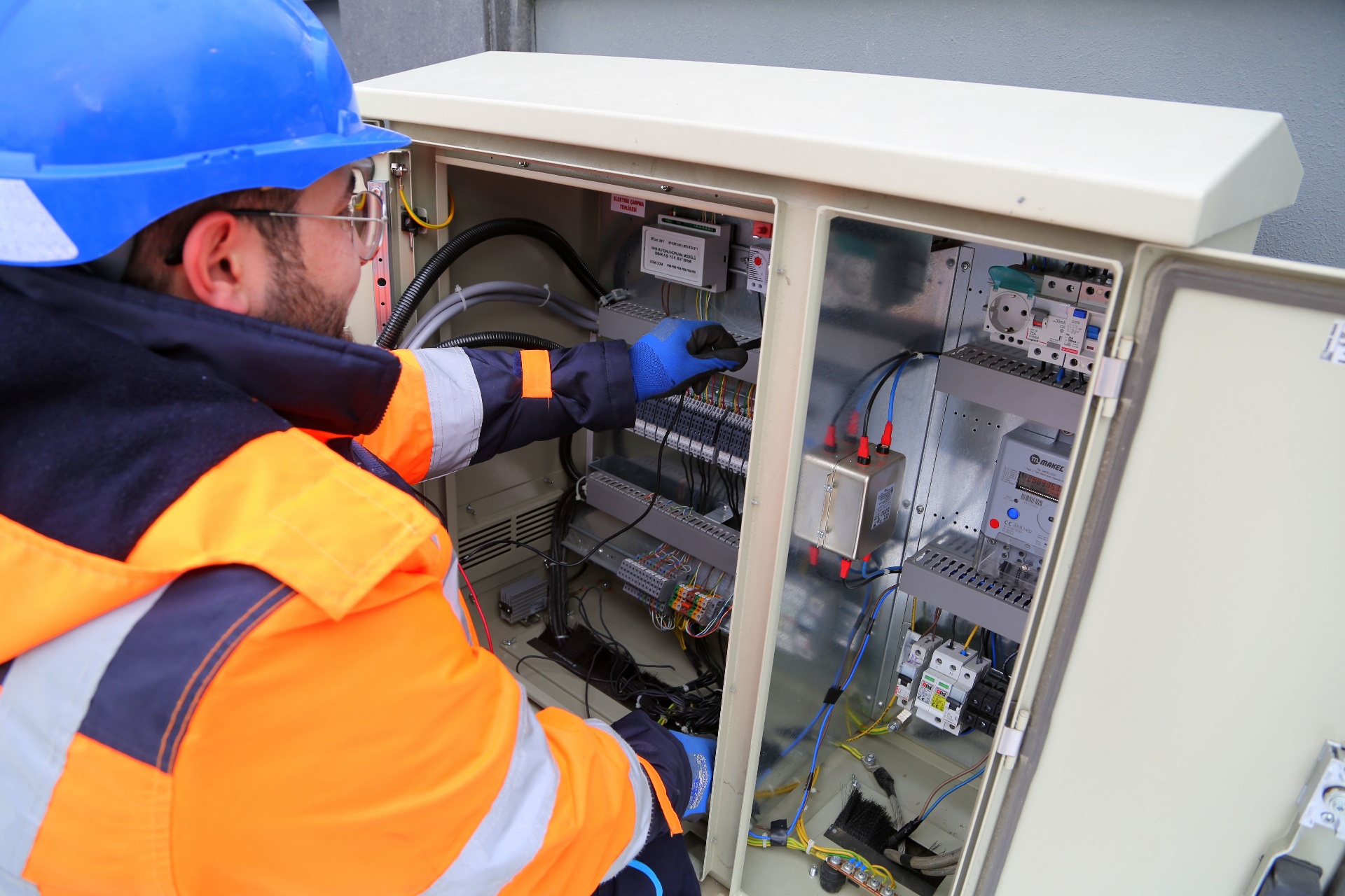 Essex electrician in orange hi-vis wiring an outdoor control panel with RCD breakers and meter - local SEO for electricians by Click Boosters